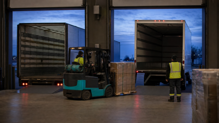 A replacement unbranded truck recovering a stranded urgent pallet shipment at a freight yard after sunset.